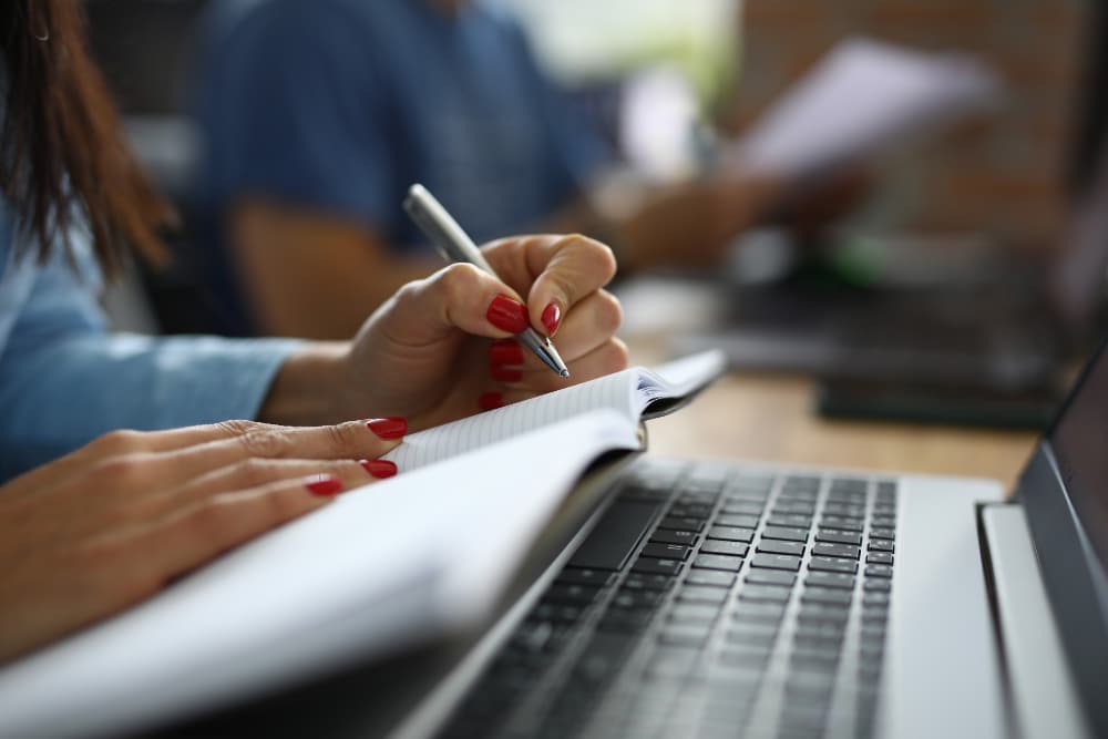 Pessoa estudando para concurso com caderno e laptop aberto na mesa